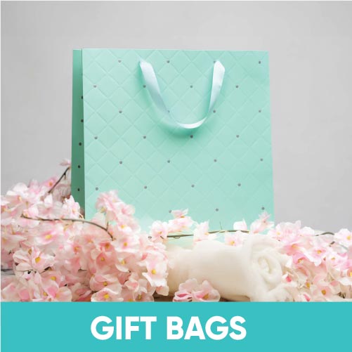 Emartbuy Gifting presents an elegant mint green gift bag adorned with white polka dots, surrounded by delicate pink cherry blossoms and a white ribbon, set against a neutral backdrop.