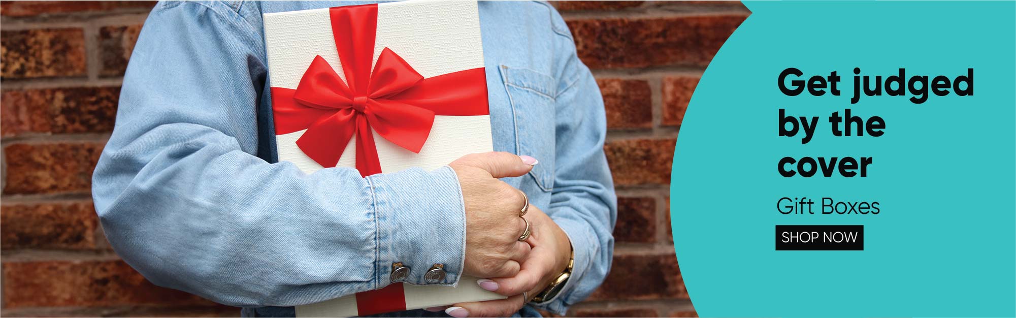 Person Holding Gift Box with Red Ribbon in Front of Brick Wall | Emartbuy Gifting